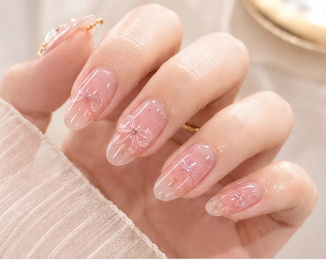 Close-up of almond nails in a sheer pink finish with small pearl bow details